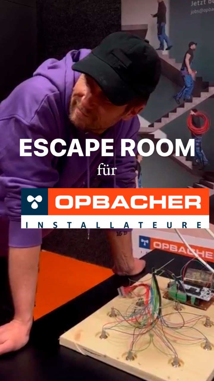 Ein Mann in violettem Kapuzenpullover und schwarzer Kappe beugt sich über einen Tisch mit einer verdrahteten Schaltung; großes Overlay-Logo mit dem Schriftzug 'ESCAPE ROOM für OPBACHER INSTALLATEURE'.
